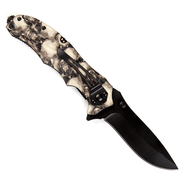 Navaja plegable metalica con hoja negra, clip para cinturon y empunadura con motivo de calaveras