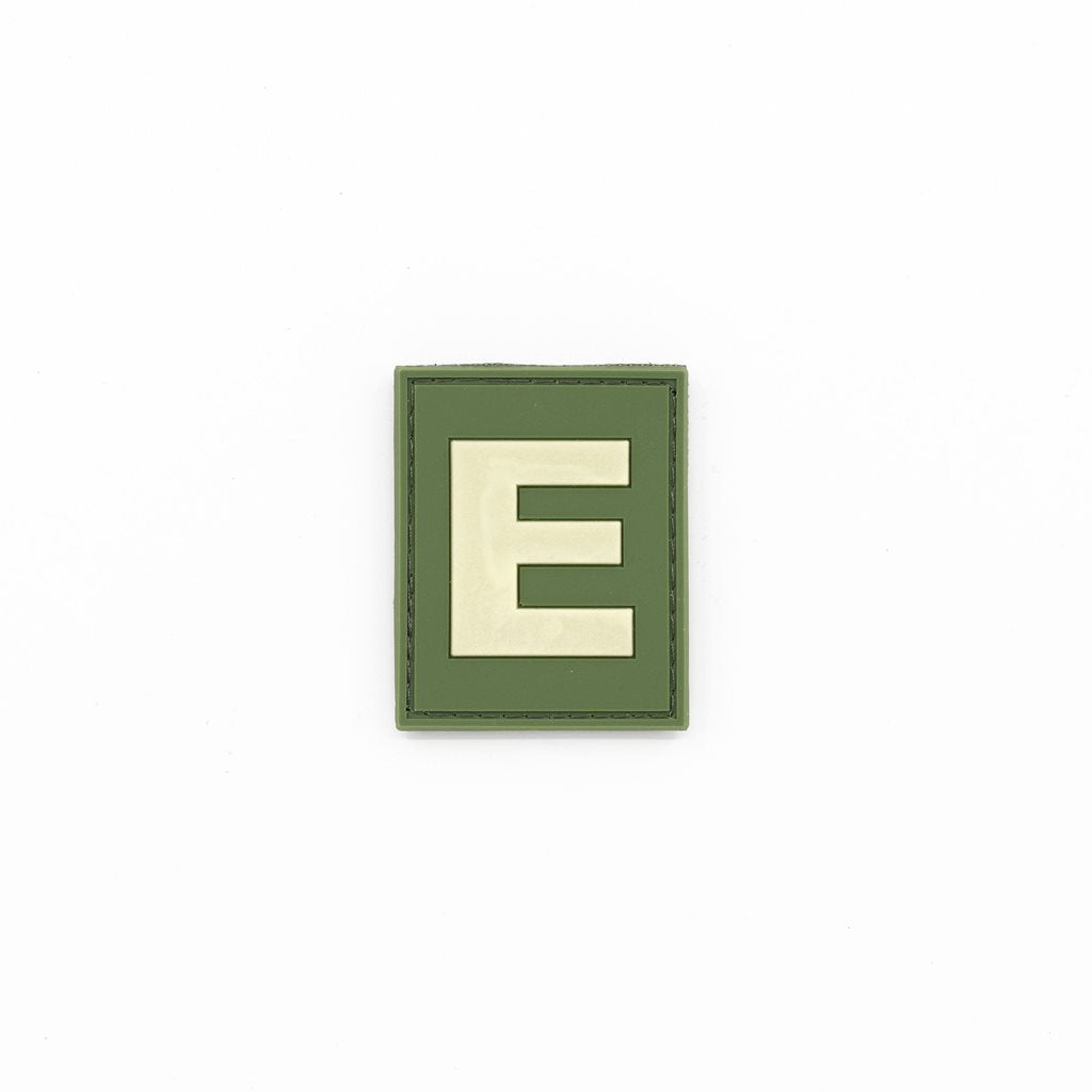 Parche identificativo 'E' verde con velcro, plástico y fosforescente (brilla en la oscuridad)
